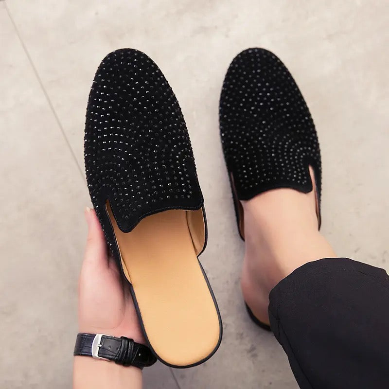 Top view of black mule loafers for men, held up by a person